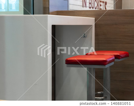 Minimalist white tall table with two bright red bar stools in a modern interior setting, offering a sleek and clean dining area for fast food customers seeking a quick casual break Minimalist white tall table with two bright red bar stools in a modern interior setting, offering a sleek and clean dining area for fast food customers seeking a quick casual break 140881051