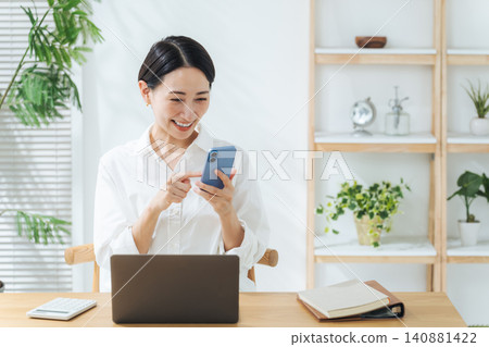 一位中年婦女一邊看著她的智慧型手機一邊微笑。應用程式、社交媒體、影片、優惠、優惠券、積分、獎勵計劃、線上購物。 一位中年婦女一邊看著她的智慧型手機一邊微笑。應用程式、社交媒體、影片、優惠、優惠券、積分、獎勵計劃、線上購物。 140881422