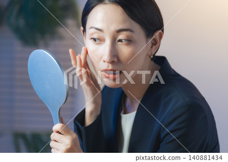 A middle-aged woman checks her skin in a dark room. Skincare, beauty, cosmetics, makeup remover, makeup removal. 140881434