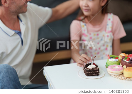 Daughter placing candle on birthday cake with father at home Daughter placing candle on birthday cake with father at home 140881503