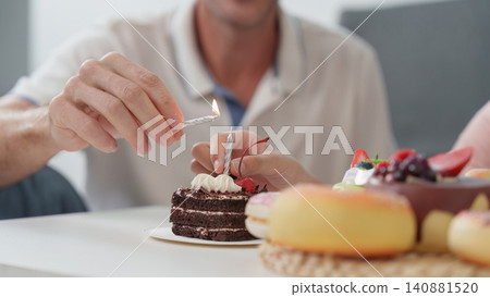 Cropped hands lighting candle on chocolate birthday cake for celebration 140881520