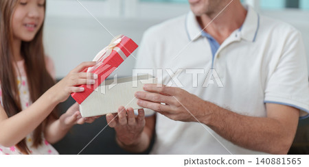 Girl giving Father's Day gift in red box to her dad at home Girl giving Father's Day gift in red box to her dad at home 140881565