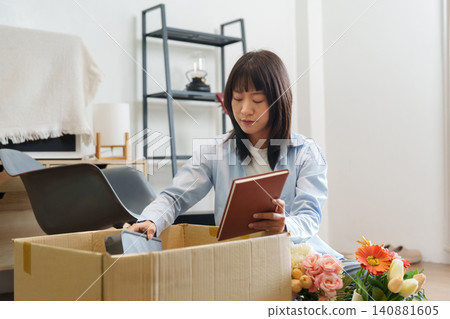 Asian woman unpacking cardboard box with notebook in new home Asian woman unpacking cardboard box with notebook in new home 140881605