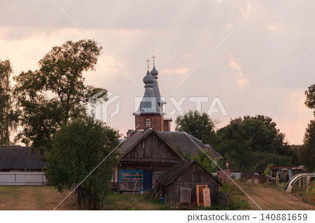 Rural landscape at dusk featuring an old wooden house and a church with onion domes in a quiet village Rural landscape at dusk featuring an old wooden house and a church with onion domes in a quiet village 140881659