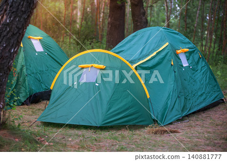 Camping tents set up in a forest during sunset with greenery surrounding the area Camping tents set up in a forest during sunset with greenery surrounding the area 140881777