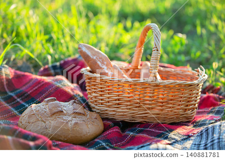 Picnic basket with freshly baked bread placed on a checkered blanket in a sunny meadow setting Picnic basket with freshly baked bread placed on a checkered blanket in a sunny meadow setting 140881781