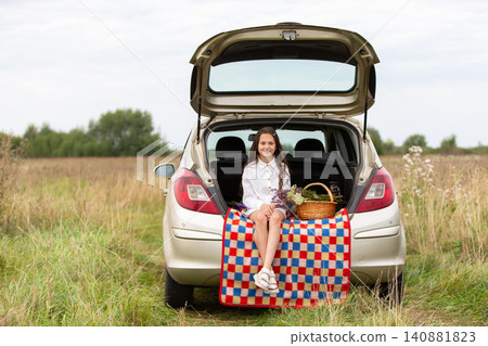 Girl enjoys a picnic by her car in a grassy field on a calm day Girl enjoys a picnic by her car in a grassy field on a calm day 140881823