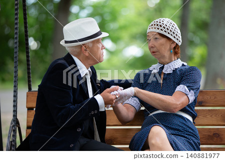 Elderly couple seated on a park bench sharing a heartfelt conversation in a serene outdoor setting during daytime 140881977