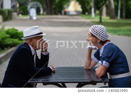 Elderly couple enjoying conversation at a park table during a sunny afternoon in summer Elderly couple enjoying conversation at a park table during a sunny afternoon in summer 140881995