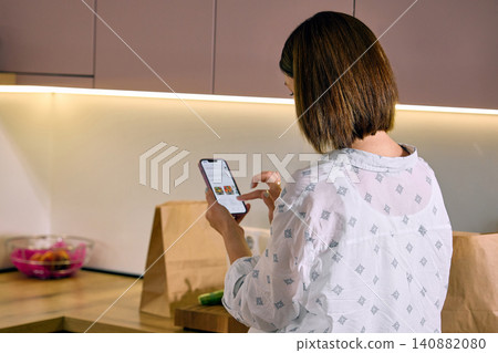 Woman selecting groceries on smartphone in home kitchen. Woman selecting groceries on smartphone in home kitchen. 140882080