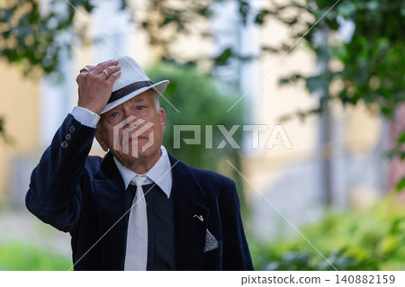 Man adjusts his hat while standing in a lush green garden during a sunny afternoon Man adjusts his hat while standing in a lush green garden during a sunny afternoon 140882159