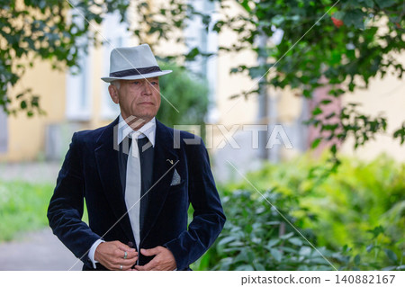 An elderly man in official clothes confidently walks along an open path surrounded by herbs An elderly man in official clothes confidently walks along an open path surrounded by herbs 140882167