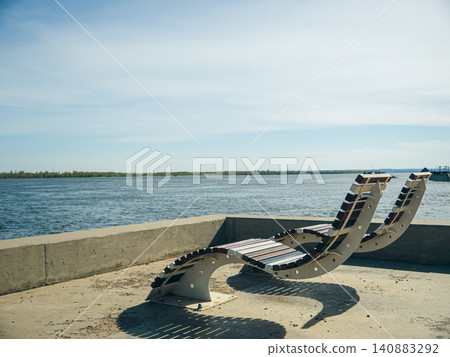 Sun loungers stand on a sun-drenched concrete pier on the Volga River embankment Sun loungers stand on a sun-drenched concrete pier on the Volga River embankment 140883292
