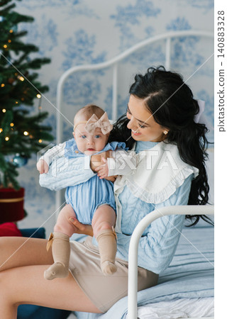 Mother Holding Baby Girl near Christmas Tree Indoors Mother Holding Baby Girl near Christmas Tree Indoors 140883328