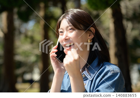 Japanese woman makes a triumphant gesture while talking on the phone in a park Japanese woman makes a triumphant gesture while talking on the phone in a park 140883655