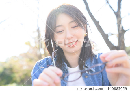 Japanese woman takes off her glasses in a park Japanese woman takes off her glasses in a park 140883659
