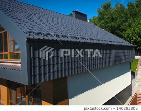 House with a gray metal roof. Corrugated metal roof and metal roofing. Modern roof made of metal. House with a gray metal roof. Corrugated metal roof and metal roofing. Modern roof made of metal. 140883808