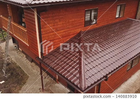 House with a brown metal roof.Corrugated metal roof and metal roofing. Modern roof made of metal. House with a brown metal roof.Corrugated metal roof and metal roofing. Modern roof made of metal. 140883910