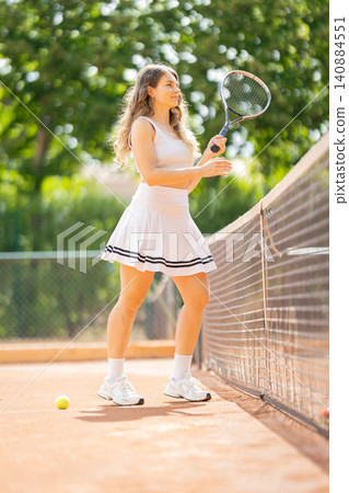 Tennis player practices on court during sunny day with green trees in background Tennis player practices on court during sunny day with green trees in background 140884551