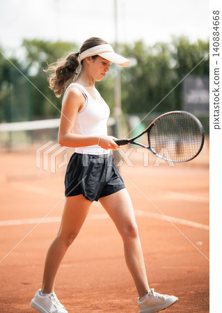 Female tennis player walks on clay court during practice session in the afternoon at local sports club Female tennis player walks on clay court during practice session in the afternoon at local sports club 140884668