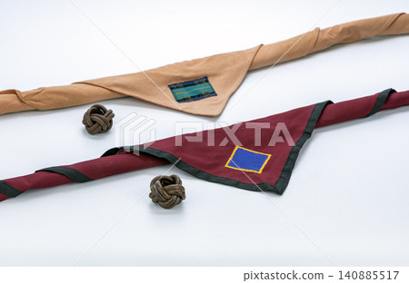 Traditional Thai Boy Scout uniform neckerchiefs in tan and burgundy maroon featuring colorful patches paired with handmade leather Turk's Head knot woggles displayed neatly on clean white background 140885517