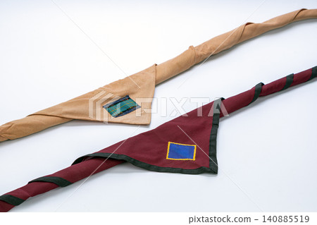 Two Thai scout neckerchief scarves in tan beige and dark maroon red colors featuring blue and tartan plaid fabric patches with rolled woggle knots arranged neatly on clean white studio background Two Thai scout neckerchief scarves in tan beige and dark maroon red colors featuring blue and tartan plaid fabric patches with rolled woggle knots arranged neatly on clean white studio background 140885519