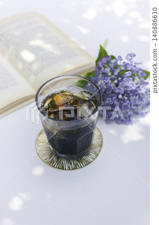 一張令人耳目一新的餐桌照片,讓人聯想到夏日閱讀時光:陽光透過樹木和繡球花灑在冰咖啡上。 一張令人耳目一新的餐桌照片,讓人聯想到夏日閱讀時光:陽光透過樹木和繡球花灑在冰咖啡上。 140886610