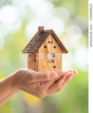 Hands holding a miniature model of a house against a blurred background Hands holding a miniature model of a house against a blurred background 140886624