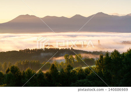 Early morning in Biei, Hokkaido: A breathtaking and fantastical view of the sea of clouds and the Tokachi mountain range bathed in the morning glow. Early morning in Biei, Hokkaido: A breathtaking and fantastical view of the sea of clouds and the Tokachi mountain range bathed in the morning glow. 140886989