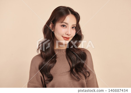 A beautiful young Asian woman with clean, fresh skin against a beige background. Skincare, facial treatment, cosmetology, beauty, and spa. An elegant portrait of an Asian woman. 140887434