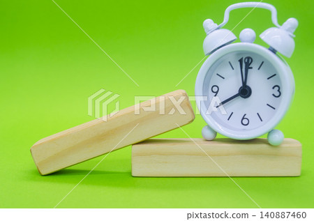 Angled wooden display blocks paired with a vintage alarm clock on a vivid green background for creative product displays. 140887460