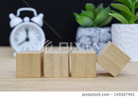 Wooden cube podium with vintage alarm clock and potted plant creating a modern natural product display setting. 140887462