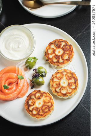Savory Syrniki with Smoked Salmon, Olives and Sour Cream on White Plate Savory Syrniki with Smoked Salmon, Olives and Sour Cream on White Plate 140887675