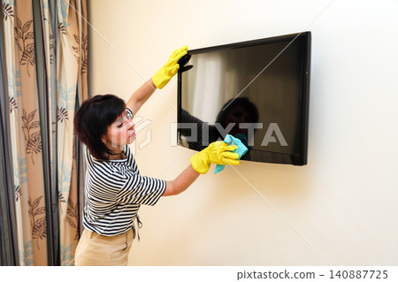 Homemaker in casual clothes wiping dust and dirt off a television screen during routine household cleaning Homemaker in casual clothes wiping dust and dirt off a television screen during routine household cleaning 140887725
