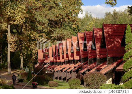 A row of quaint stone and wood structures with distinctive red tiled roofs nestled amongst trees displaying vibrant fall foliage under a bright sky A row of quaint stone and wood structures with distinctive red tiled roofs nestled amongst trees displaying vibrant fall foliage under a bright sky 140887814