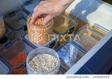 Food storage containers. Woman's hand takes a handful of pearl barley from an open container. Food storage containers. Woman's hand takes a handful of pearl barley from an open container. 140888419