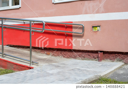 Disabled call button assistance system is installed near an accessible wheelchair ramp. Yellow handicap symbol sign sits on a textured concrete wall 140888421