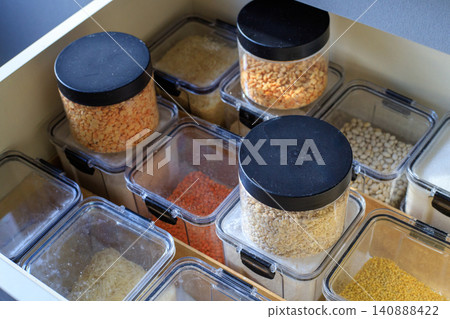 Clear plastic containers are filled with flour and grains. Well-organized kitchen cabinet drawer holds various dry goods 140888422