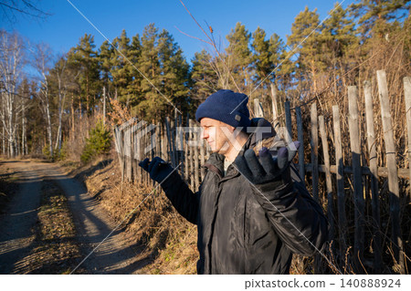 Man talking on smartphone outdoors. Confused male with blue hat standing near fence in nature. Communication problem and connection issue. Mobile phone usage in rural environment. Man talking on smartphone outdoors. Confused male with blue hat standing near fence in nature. Communication problem and connection issue. Mobile phone usage in rural environment. 140888924