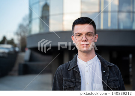 Young entrepreneur standing outside a modern office building in an urban business district wearing eyeglasses. Professional leadership and entrepreneurial career growth Young entrepreneur standing outside a modern office building in an urban business district wearing eyeglasses. Professional leadership and entrepreneurial career growth 140889212
