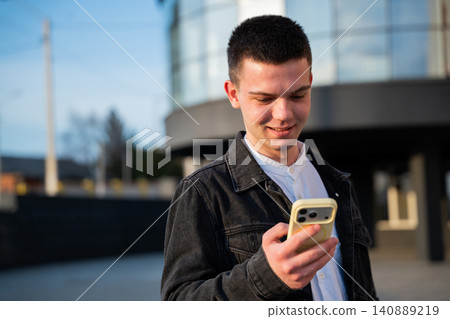 Young man using a smartphone outside a modern office building during the workday. Mobile communication and digital business connectivity Young man using a smartphone outside a modern office building during the workday. Mobile communication and digital business connectivity 140889219