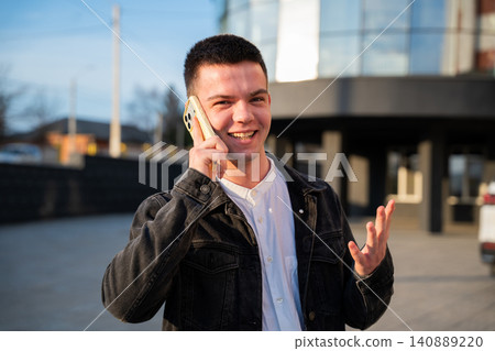 Young man talking on a smartphone outside a modern office building during the workday. Mobile communication and everyday business connectivity Young man talking on a smartphone outside a modern office building during the workday. Mobile communication and everyday business connectivity 140889220