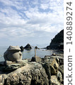 A stunning view of a frog statue standing on the beach and the Meoto Iwa (Husband and Wife Rocks) against the blue sky. 140889274