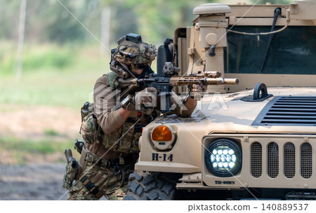 One army man point gun to enemy direction and lean on front hood of High Mobility Multipurpose Wheeled Vehicle to practice of fight with enemy. 140889537