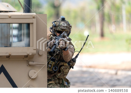 One army man point gun to enemy direction and lean on front left door of High Mobility Multipurpose Wheeled Vehicle to practice of fight with enemy. 140889538