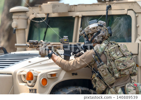 One army man point gun to enemy direction and lean on front hood of High Mobility Multipurpose Wheeled Vehicle to practice of fight with enemy. 140889539