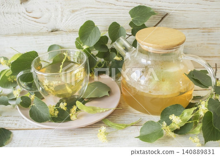 Linden tea in a glass cup with fresh linden flowers, on a wooden background. Medicinal herbal tea. Linden tea in a glass cup with fresh linden flowers, on a wooden background. Medicinal herbal tea. 140889831
