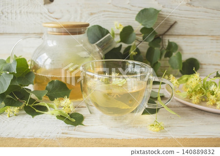 Linden tea in a glass cup with fresh linden flowers, on a wooden background. Medicinal herbal tea. Linden tea in a glass cup with fresh linden flowers, on a wooden background. Medicinal herbal tea. 140889832