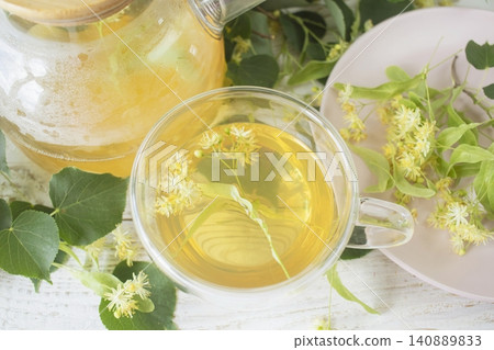 Linden tea in a glass cup with fresh linden flowers, on a wooden background. Medicinal herbal tea. 140889833