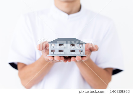 一位身穿白大褂的中年男子,手裡拿著一棟公寓大樓的模型。 一位身穿白大褂的中年男子,手裡拿著一棟公寓大樓的模型。 140889863